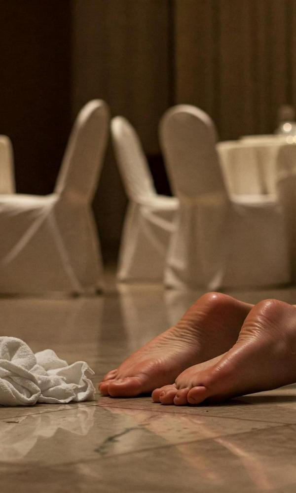 Bare, glistening feet beside a fallen towel on a marble ballroom floor. No motion. No resistance. Just surrender, witnessed.